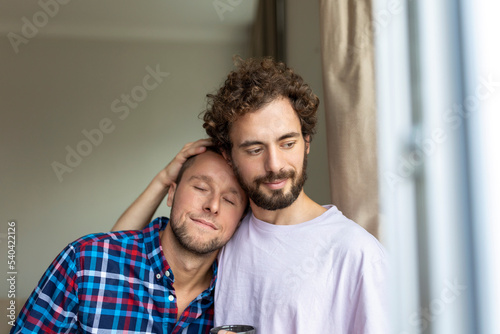 Cheerful young gay couple sitting together. Two affectionate male lovers smiling cheerfully while embracing each other. Young gay coupe being romantic. © Graphicroyalty