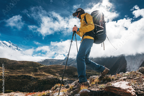 Outdoor tourist traveling along high altitude mountains wearing yellow jacket and professional backpack. Young solo hiker walk across sunny mountain track