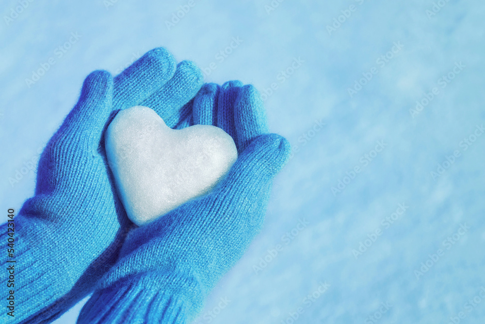 Female hands in knitted gloves with heart of snow in winter day. Love concept. Valentine day background.	