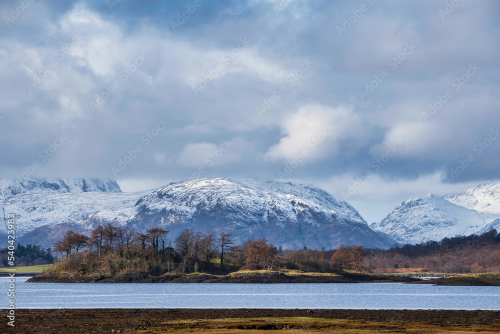 Beautiful Winter landscape view along Loch Leven in Scotland towards snowcapped mountains in distance with dramatic sky