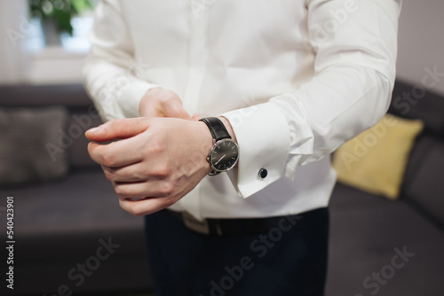 Putting on a watch. Businessman in white shirt and suit trousers. Groom getting ready for the wedding. Wearing clothes background. Dressing up male fashion. Business fashion hotel room. Checking time.