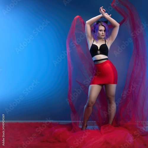 sexy girl in a red skirt and a bustier poses erotically with a transparent fabric