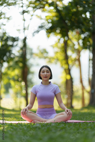 Attractive Asian woman in sportswear practicing yoga in the outdoor park