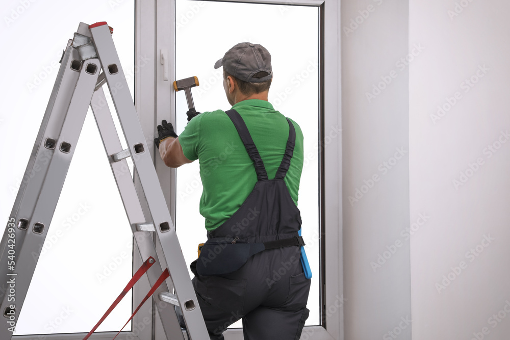 Worker using hammer for double glazing window installation indoors, back view