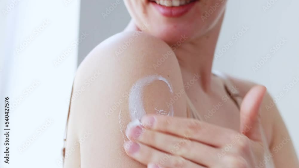Smiling beautiful young caucasian woman apply moisturizing body lotion on shoulder, do daily routine nourishing smoothing cream after shower.Beauty and healthy skin care treatment concept.Slow motion