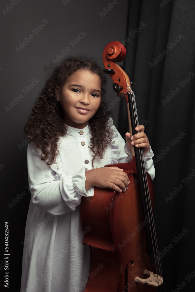 Beautiful girl in a stylish dress stands with a cello. Beautiful girl in a stylish dress stands with a cello.