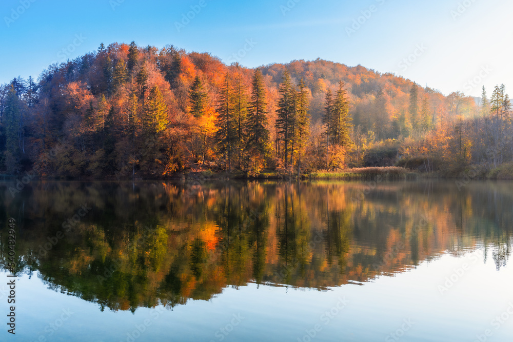 Orange autumn on lake. Beautiful peaceful autumn landscape with beautiful trees and a lake. Reflection in the water of colorful trees