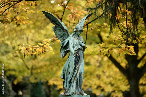 Fotografía beautiful old angel with wings in front of golden autumn leaves in a cemetery