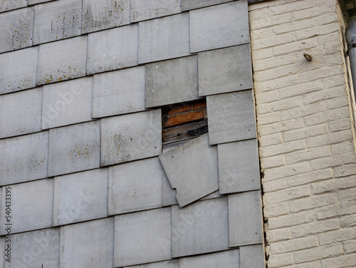 Broken asbestos facade with a damaged sheet hanging down. Toxic material on a building exterior. It can be dangerous for humans and the environment. This construction material was used in East Germany