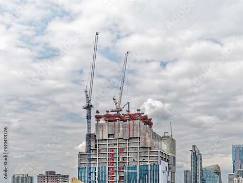 Under Construction Building with Cranes and Workers Against Cloudy Sky