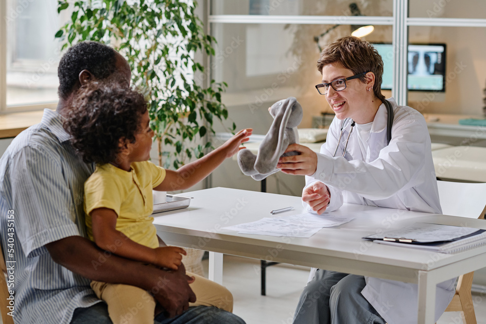 Fototapeta premium Female doctor showing the toy to little child while they sitting at office during visit at hospital