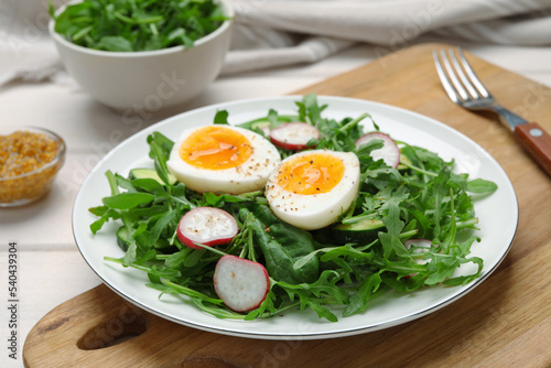 Delicious salad with boiled egg, vegetables and arugula on wooden board, closeup