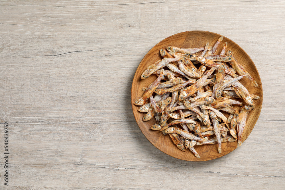 Plate of tasty dried anchovies on light wooden table, top view. Space for text Plate of tasty dried anchovies on light wooden table, top view. Space for text
