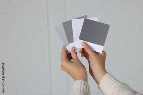 Woman with color sample cards choosing paint shade for wall indoors, closeup. Interior design