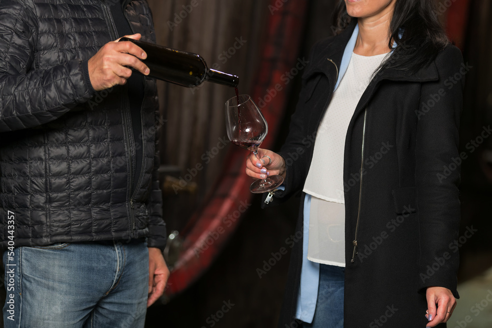 Cellar master, or winemaker pouring red wine for a woman to taste it and explaining wine varietals to her Cellar master, or winemaker pouring red wine for a woman to taste it and explaining wine varietals to her
