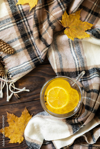Seasonal autumn concept with drink. Cup of hot sea ​​​​buckthorn tea with lemon, warm scarf and maple leaves on rustic background, creative flat lay. View from above.