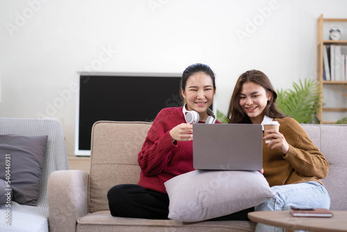 Two asian young woman happy smiling and using computer laptop on couch in living room at home