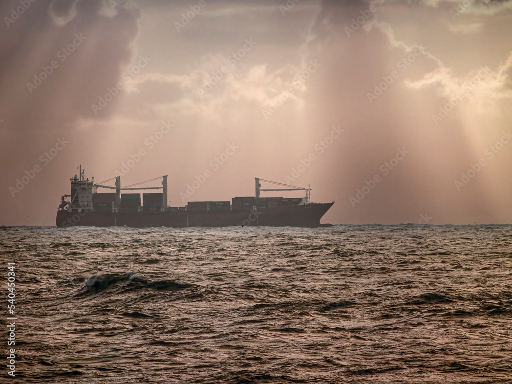 Commercial ship against dramatic cloudy sky with sunbeams