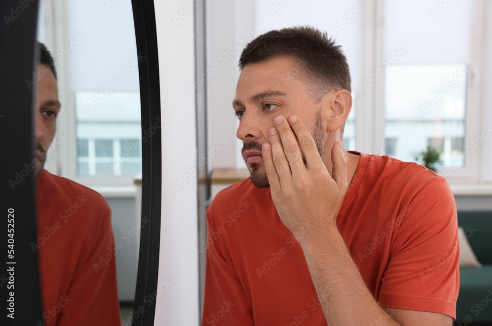 Sleep deprived man looking at himself in mirror indoors Sleep deprived man looking at himself in mirror indoors