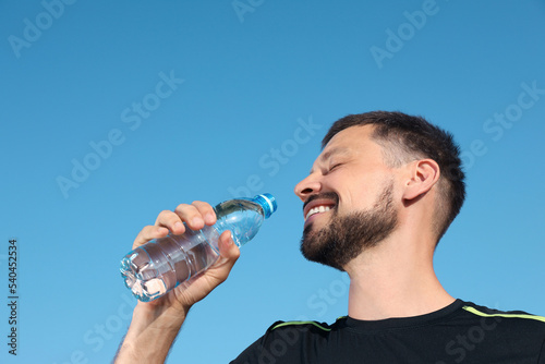 Happy man drinking water against blue sky on hot summer day. Refreshing drink