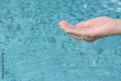 Water pouring into girl's hand above pool, closeup. Space for text