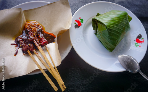 Sate maranggi (sweet marinated beef skewers) served with rice wrapped in banana leaves and sliced cucumber. Sate maranggi with sambal oncom or oncom sauce. indonesian traditional food photo