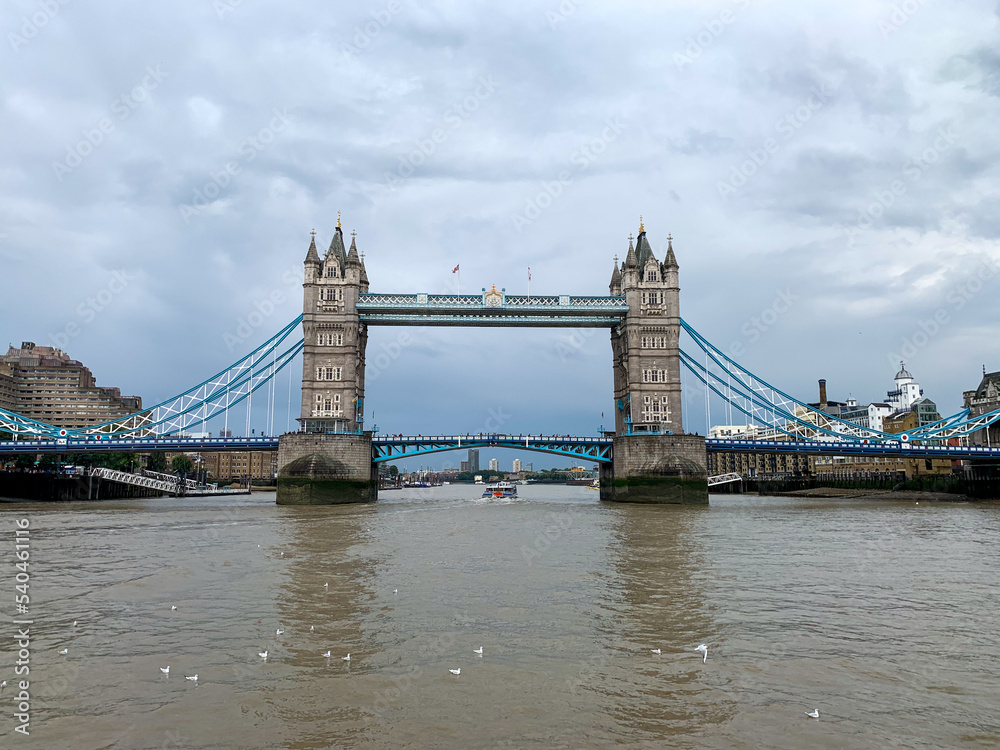 Fototapeta premium The historic Tower Bridge stands like a huge rock in the surf of the London Thames, a ship passes under it, while at the same moment thousands of people can cross the river with the help of the bridge