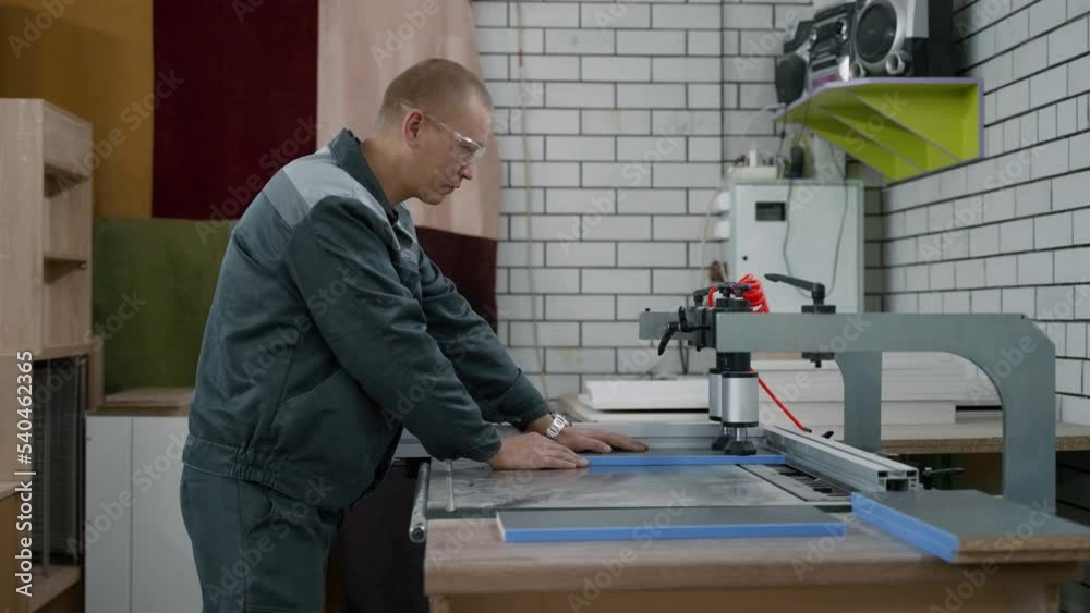 The furniture maker, wearing safety glasses and a uniform, makes holes in the parts on a special machine. The furniture maker, wearing safety glasses and a uniform, makes holes in the parts on a special machine.