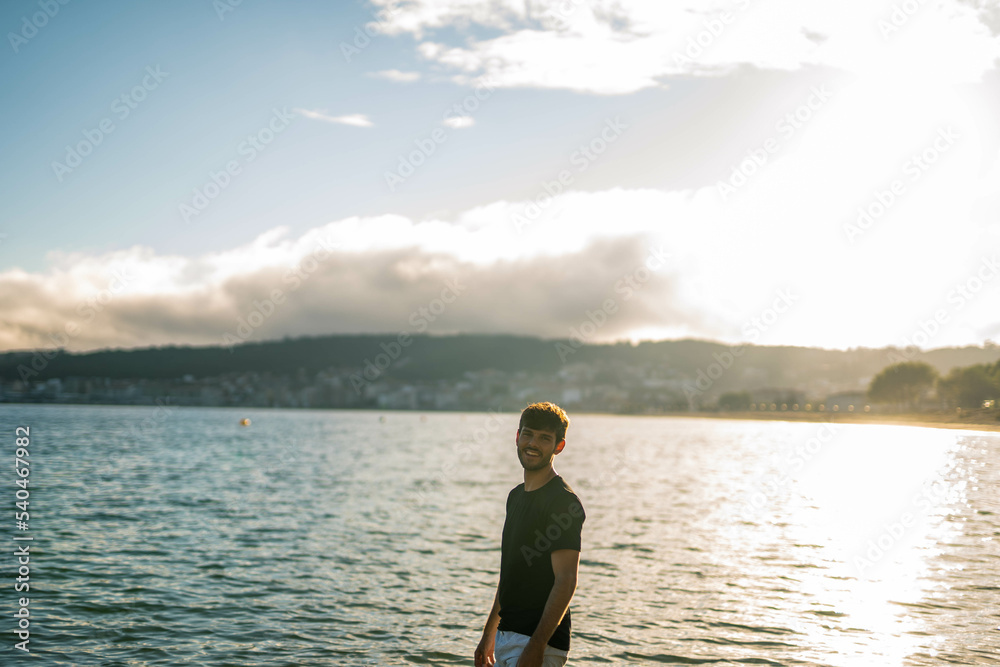 Young Caucasian man staring at the camera in the beach at sunset