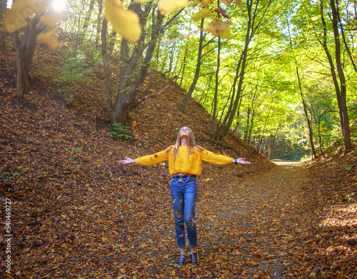 Young woman with backpack walks through the city forest park and enjoys nature on autumn sunny day © okostia