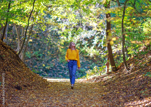 Young woman with backpack walks through the city forest park and enjoys nature on autumn sunny day © okostia