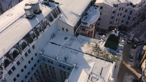 Aerial top view of sweepers cleaning roof after snowfall. European buildigs after heavy snow. photo