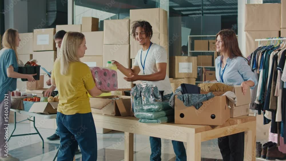 The Concept of Giving:Positive Group of Young Adult Volunteers Serving Humanitarian Aid to Refugees and Immigrants. Humanitarian Aid Charity Workers Serve Meals and Hygiene Products to People in Need. The Concept of Giving:Positive Group of Young Adult Volunteers Serving Humanitarian Aid to Refugees and Immigrants. Humanitarian Aid Charity Workers Serve Meals and Hygiene Products to People in Need.