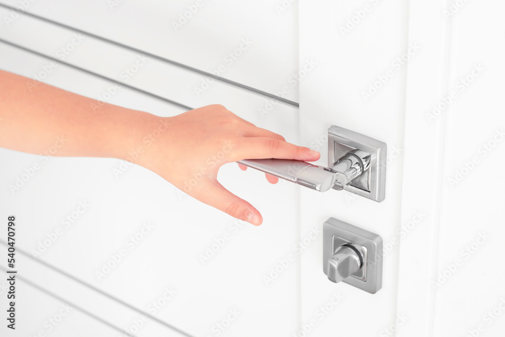 A child's hand lies relaxed on the metal handle of an interior door. A child's hand lies relaxed on the metal handle of an interior door.