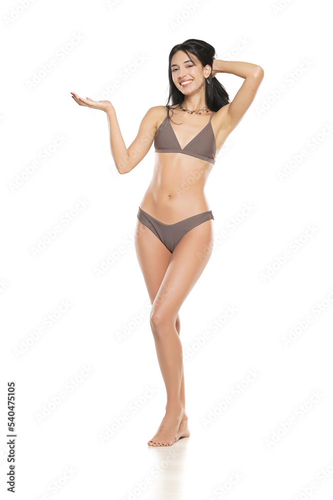 Young smiling brunette woman in bikini swimsuit advertising imaginary object  on her hand on a white background. Stock Photo | Adobe Stock