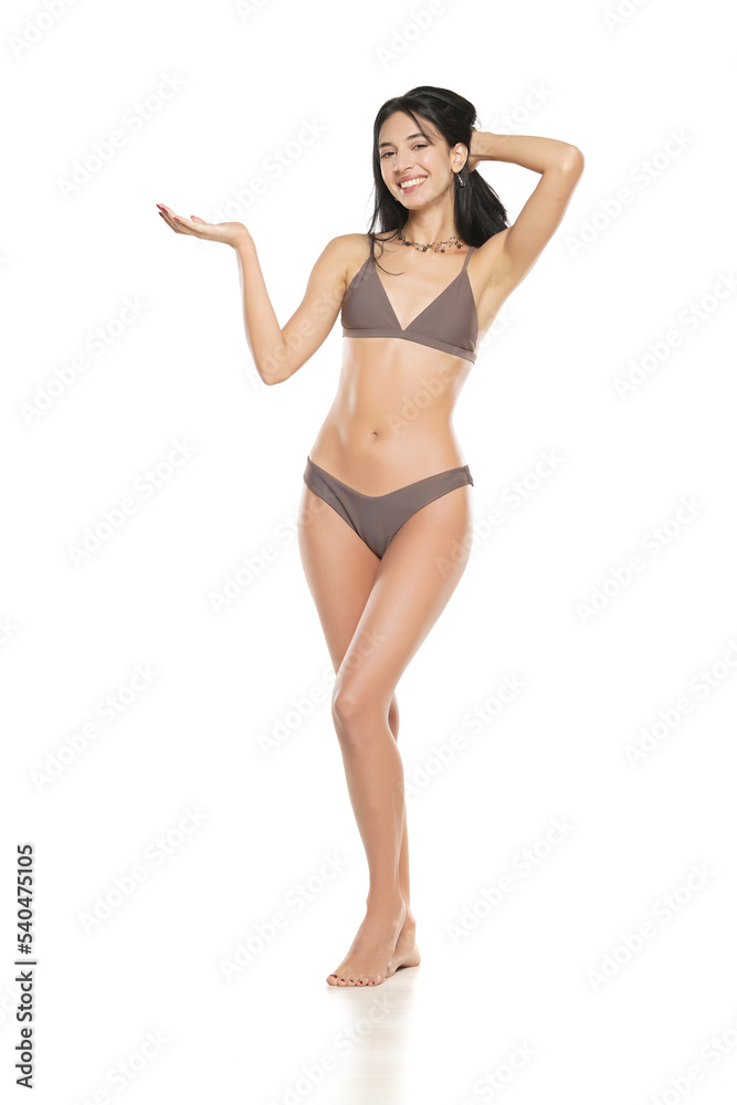Young smiling brunette woman in bikini swimsuit advertising imaginary object on her hand on a white background.
