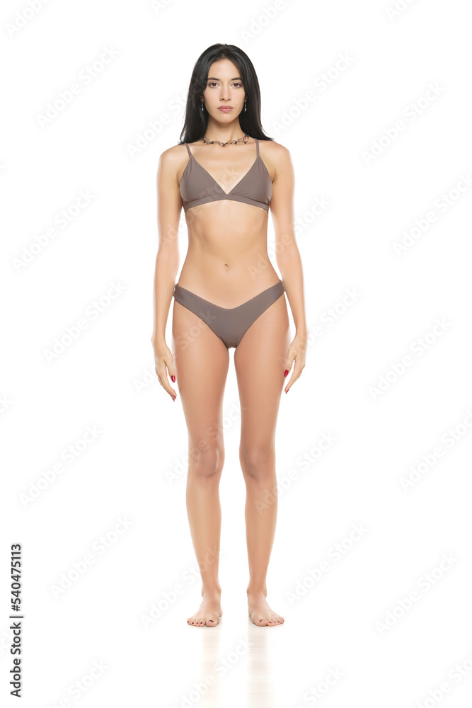 Young brunette woman in bikini swimsuit posing on a white background.