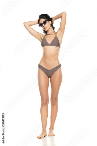 Young brunette woman in bikini swimsuit and sunglasses posing on a white background. © vladimirfloyd