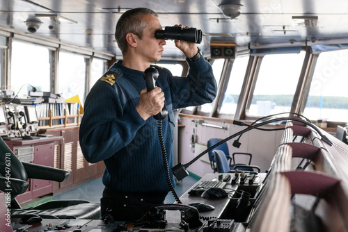 Deck officer with binoculars on navigational bridge. Seaman on board of vessel. Commercial shipping. Cargo ship. photo