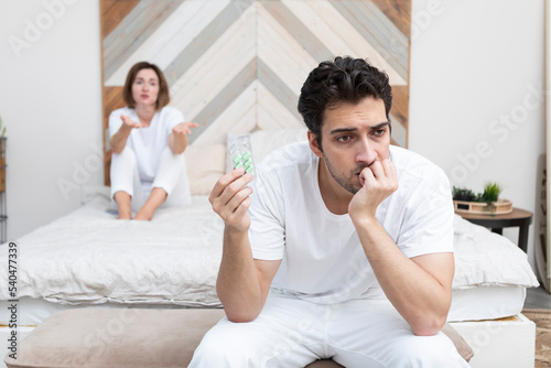 Frustrated and depressed man sitting on the edge of the bed after conflict with his wife because of his erectile dysfunction problem. He holding pills which did not work photo