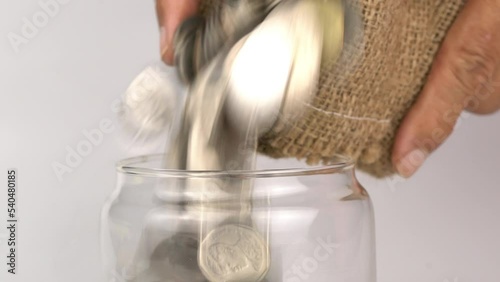Closeup view of two man hands holding and pouring different kind of coins in a sack into transparent glass jar. photo