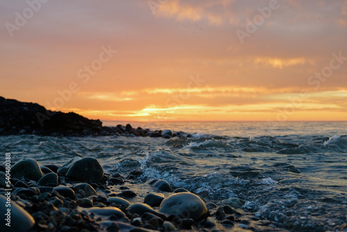Sunset on the rocky beach with sea waves and orange sky