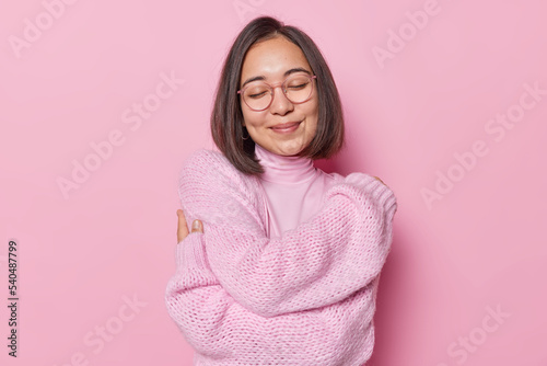 Fototapeta Tender Asian woman with dark hair embraces herself closes eyes and smiles lovely