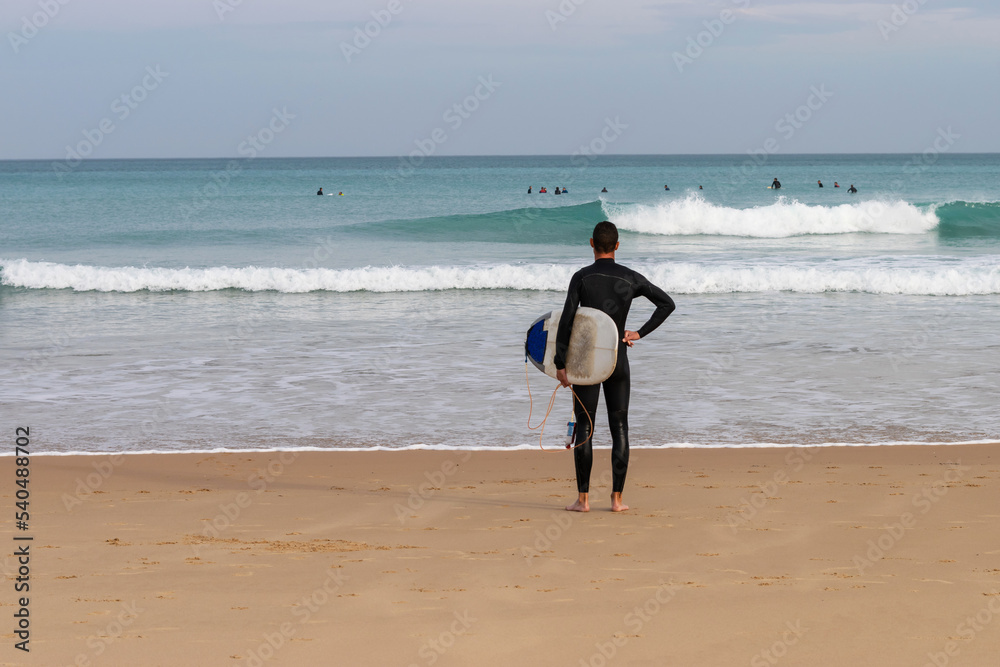 Surfer on the beach watches his friends on the waves Surfer on the beach watches his friends on the waves