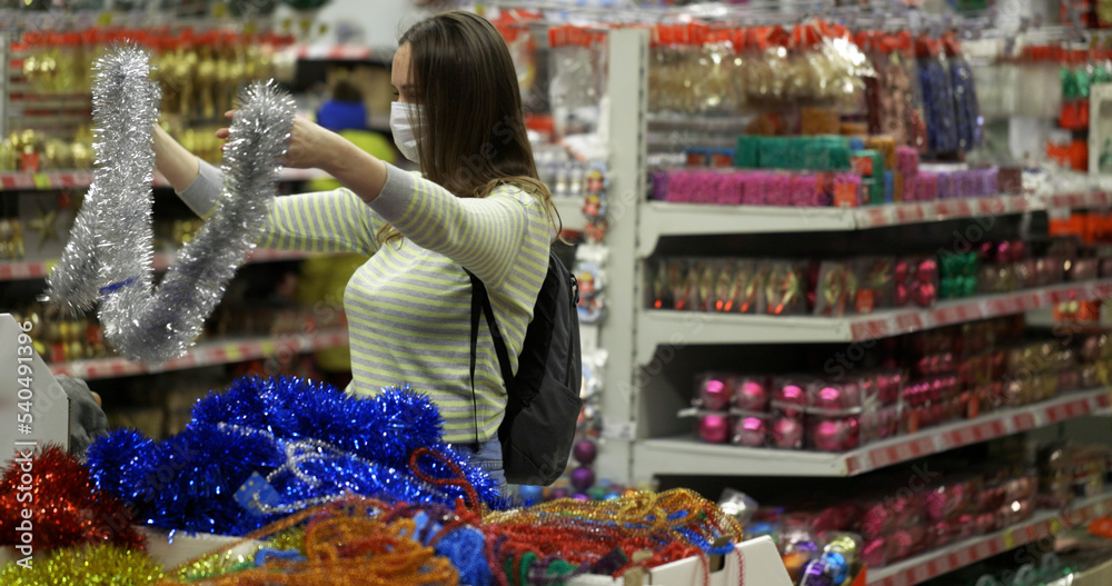 A woman in a protective mask chooses Christmas decorations and gifts at the Christmas fair. Shopping at the supermarket. Pre-holiday rush.