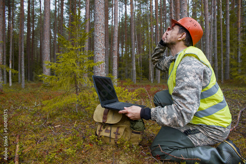 Forest worker worker works in the forest with a computer. Trees are reflected on the computer screen.
