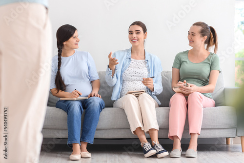 Young pregnant women with notebooks sitting on sofa at course for expectant mothers