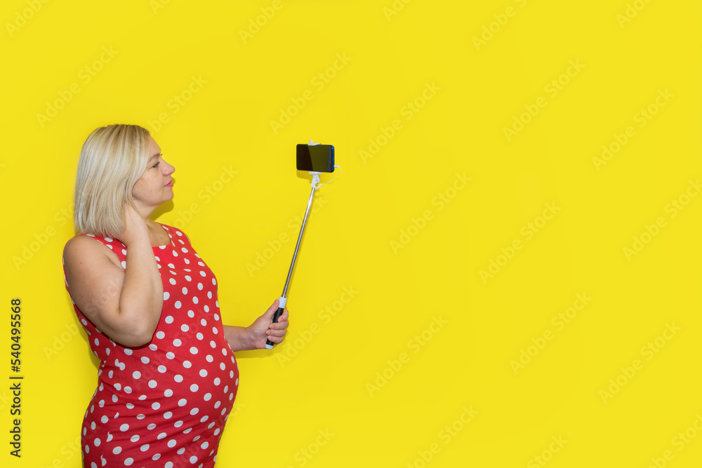 pregnant woman in a red polka dot dress takes a selfie on a yellow background with copy space pregnant woman in a red polka dot dress takes a selfie on a yellow background with copy space
