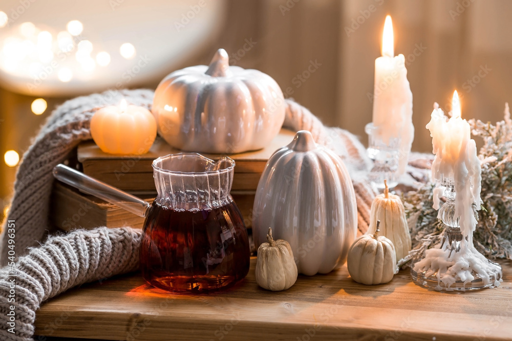 Still-life. Pumpkins, old books, hot tea, a blanket and burning pumpkin-shaped candles on a wooden table in a cozy living room. Home autumn concept. Still-life. Pumpkins, old books, hot tea, a blanket and burning pumpkin-shaped candles on a wooden table in a cozy living room. Home autumn concept.