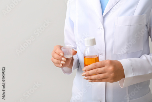 Female doctor with bottle of cough syrup and cup on grey background, closeup